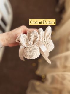 a hand holding a crochet pattern baby shoe with a bow on the side