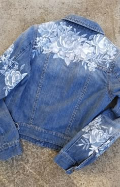 an old jean jacket with white flowers on it sitting on the ground next to a pair of scissors