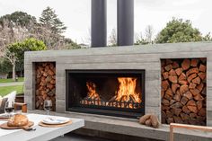 an outdoor fireplace with firewood and wine glasses on the table in front of it