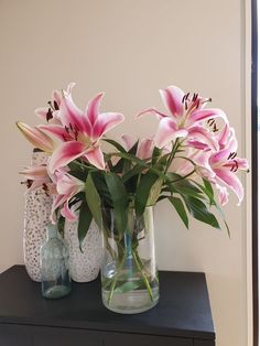 some pink flowers are in vases on a black table next to a white wall