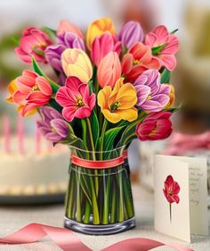 a vase filled with lots of colorful flowers next to a card and some pink candles