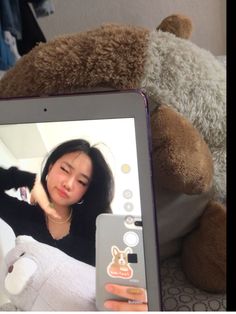 a woman is holding up a teddy bear and looking at the screen on her tablet