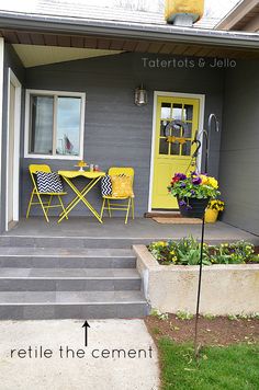 a yellow door sits in front of a gray house with steps leading up to it