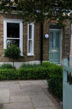 a brick house with a green door and white window panes on the side walk