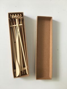 an open cardboard box with spoons and forks in it on a white table top