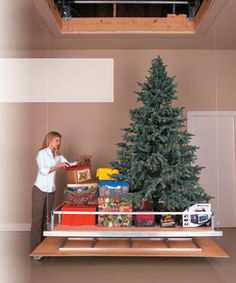 a woman standing in front of a christmas tree with presents on the shelf below it