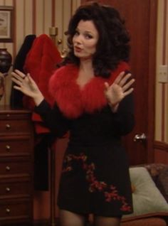 a woman in a black dress and red fur stoler standing next to a dresser