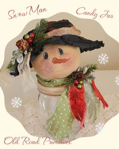 an old fashioned snowman in a glass jar with holly wreaths and pine cones