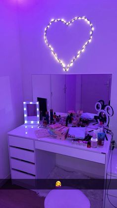 a heart shaped mirror on top of a white dresser next to a vanity with lights