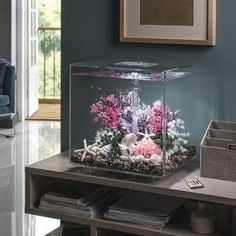 a fish tank filled with pink and white flowers on top of a wooden table next to a window