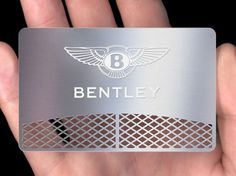 a hand holding a metal business card with the bentley logo on it's front