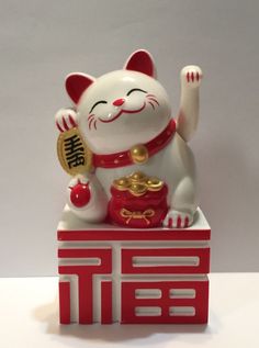 a cat figurine sitting on top of a red and white box with gold decorations