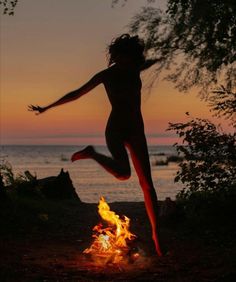 a woman jumping in the air over a fire with her arms outstretched and legs spread wide