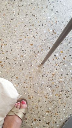 a person's feet with sandals on standing in front of a floor that has small pebbles