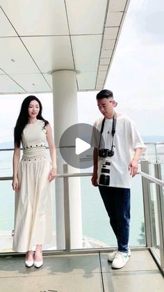 a man and woman standing next to each other on top of a building near the ocean