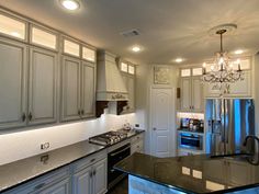 a kitchen with white cabinets and black counter tops, an island in front of the stove