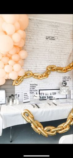 balloons are hanging from the ceiling in front of a table with white cloths and gold chains