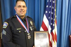 a man in uniform holding an award plaque next to two american flags and a blue curtain