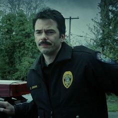 a man with a mustache standing next to a police car