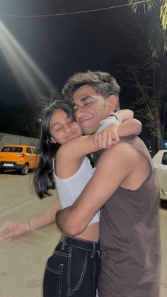 a man and woman hugging each other in the middle of a parking lot at night