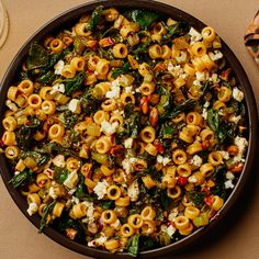 a pan filled with pasta and spinach on top of a table next to bread