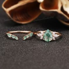 an emerald and diamond ring sitting on top of a black surface next to a shell