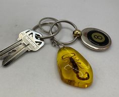 Step into the world of ancient wonders with this exquisite Scorpion in Amber Resin Keychain. Crafted with precision, this keychain features scorpion encased in high-quality amber resin, offering a glimpse into a prehistoric era. The warm, golden hues of the resin beautifully encapsulate the scorpion, creating a mesmerizing effect that is both captivating and elegant. This keychain is not only a functional accessory but also a miniature piece of art that showcases the intriguing beauty of nature. This keychain is more than just a decorative item; it symbolizes strength, protection, and resilience, attributes often associated with scorpions in various cultures. The amber resin adds a touch of ancient mystique, as amber has been prized since antiquity for its color and natural beauty. Lightwe 90s Keychains, Scorpion Keychain, Bug Keychain, Lighter Keychain, Creative Keychains, Fun Keychains, Cool Keychain, Arizona Gifts, Fit Accessories