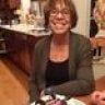 a woman sitting at a table with food in front of her and another person standing behind her