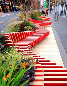 a row of red benches sitting on the side of a road next to tall buildings