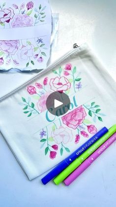 two pencils are sitting next to a clear bag with flowers on it and a video screen in the background