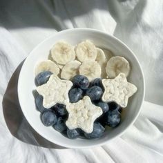 a white bowl filled with blueberries and banana slices on top of a white cloth