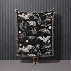 a woman standing in front of a wall holding up a black and white tapestry