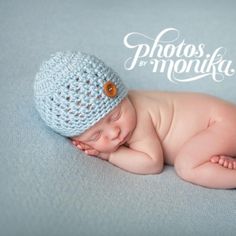 a baby wearing a blue crochet hat laying on it's side with its eyes closed