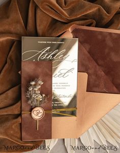 a wedding card with a feather on it sitting on top of a bed next to a pillow