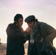 two men standing next to each other in front of the ocean with their hands together