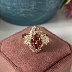 a gold ring with red and white stones in it sitting on top of a velvet box