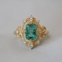 an emerald and diamond ring on a white surface with gold filigrees around it