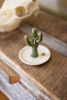 a small green cactus sitting on top of a wooden table next to a white plate