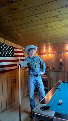 a young man standing next to a pool table with an american flag on the wall