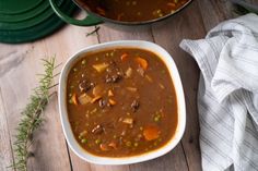 a white bowl filled with stew next to a pot of soup on top of a wooden table