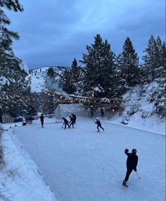 several people are skiing in the snow near some trees and string lights at night time