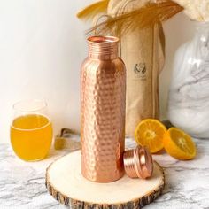 a copper colored bottle sitting on top of a wooden slice next to some oranges