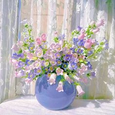 a blue vase filled with lots of purple and white flowers on top of a table