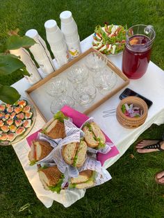 a picnic table with sandwiches, drinks and snacks on the grass in front of it