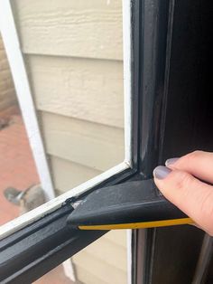 a woman's hand holding onto the side of a window with a yellow handle