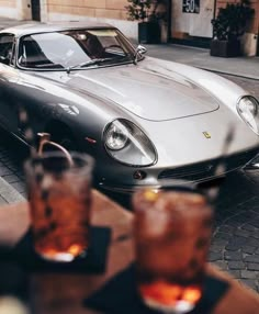 a silver sports car parked on the side of a road next to two glasses of soda