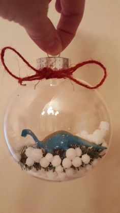 a hand holding a glass ornament with snow on it and a blue dinosaur inside