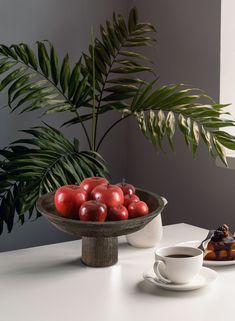 there is a bowl of cherries on the table next to a cup of coffee