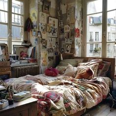 an unmade bed sitting in a bedroom next to two windows with pictures on the wall