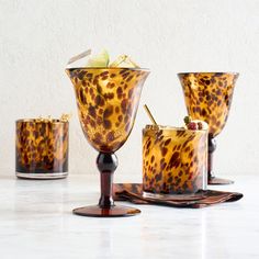 four glasses with drinks in them sitting on a marble counter top next to each other